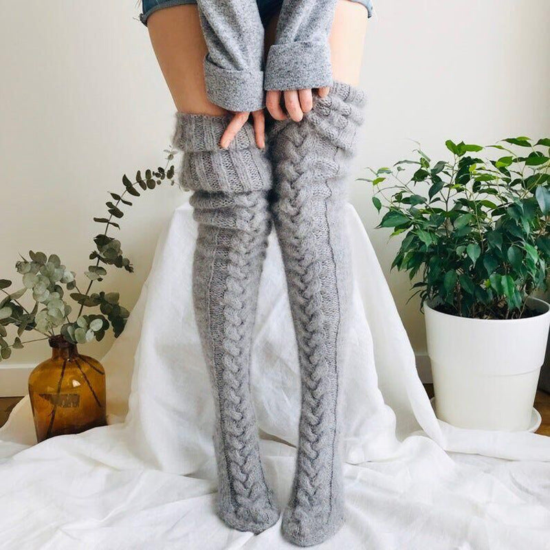 Person wearing gray knitted leg warmers with a white curtain and plants in the background