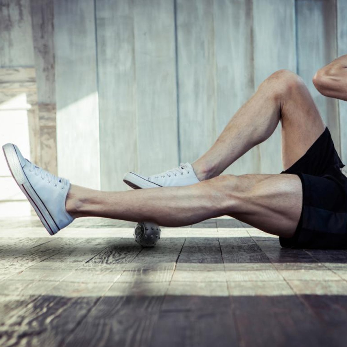 Person wearing white sneakers and black shorts sitting on a wooden floor.