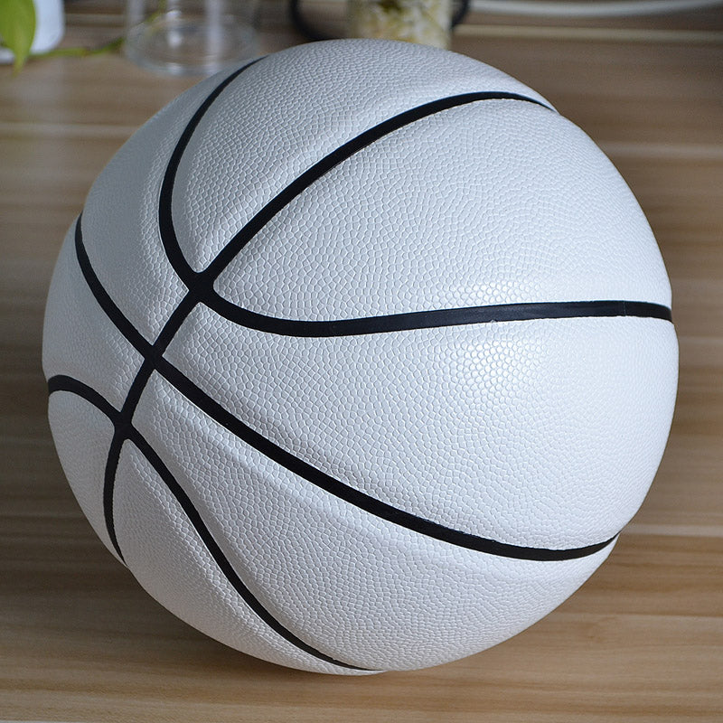A white basketball with black seams, resting on a light wooden surface.