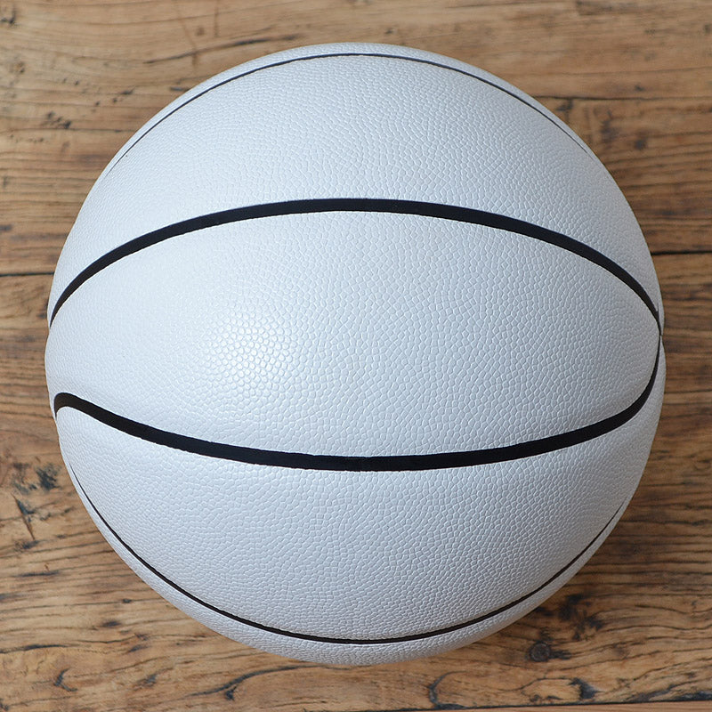 A white basketball with black seams, photographed from directly above on a rustic wooden surface.