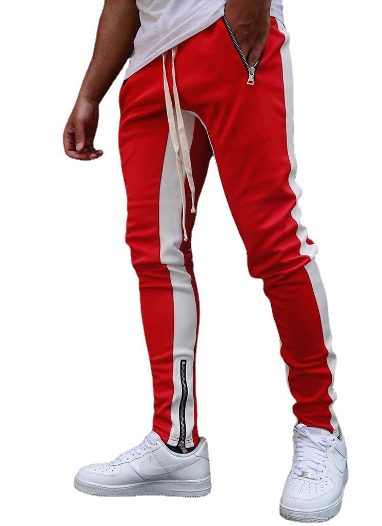 Red track pants with white stripes worn by a person on a white background