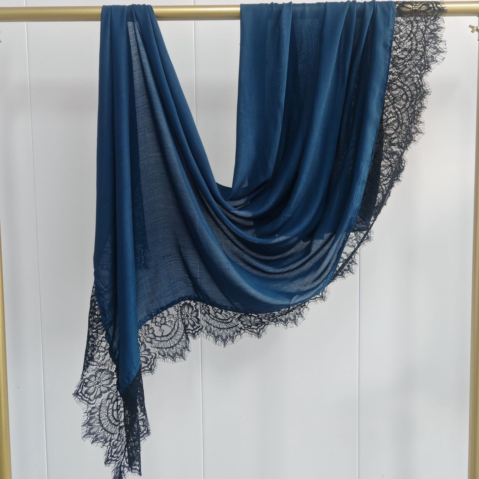 Blue scarf with black lace trim draped over a gold rod on a white background