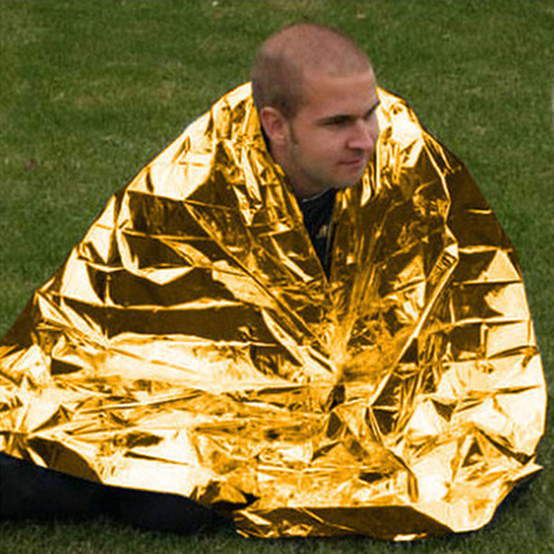Person wrapped in a gold mylar blanket on grass