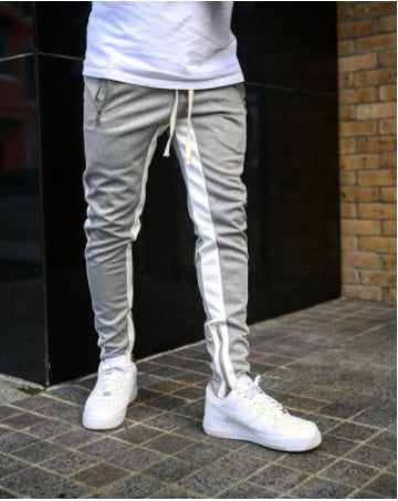 Person wearing light gray jogger pants with white stripes and white sneakers on a dark pavement.