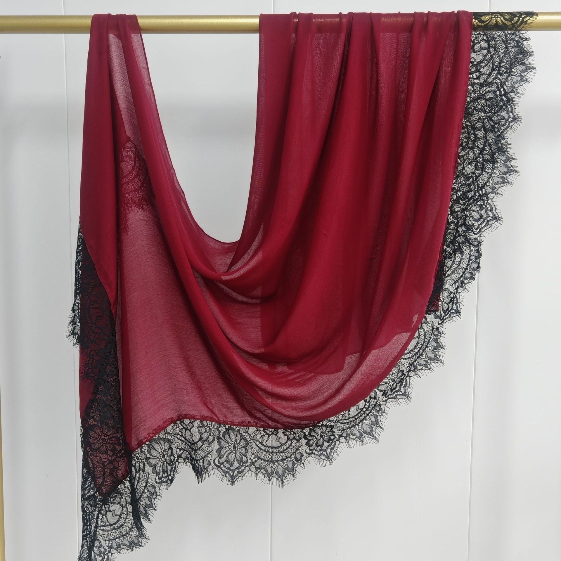 Red scarf with black lace trim draped over a gold rod on a white background