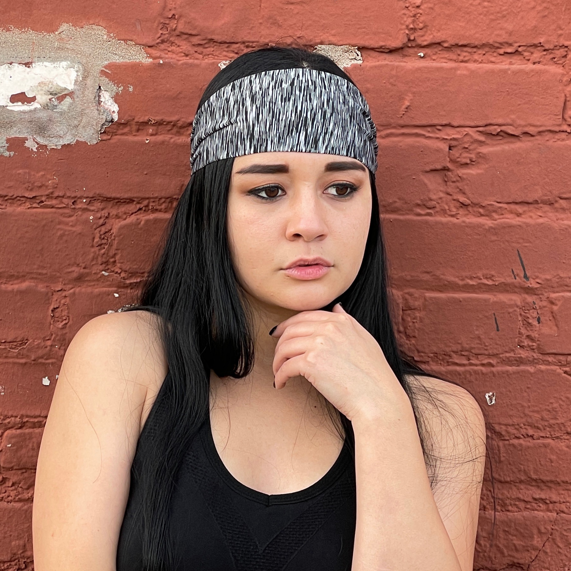 Woman wearing a black tank top and headband against a red brick wall