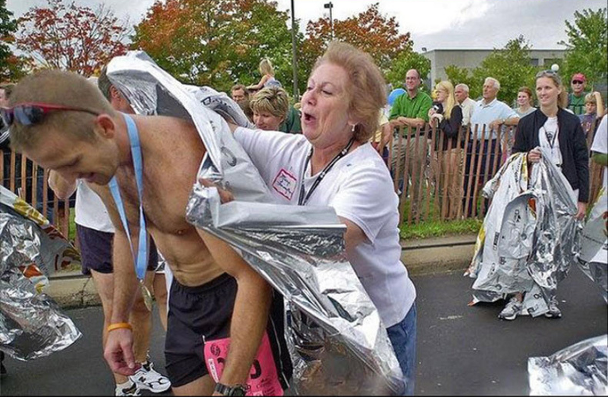 Person being wrapped in mylar by a woman with onlookers in a race setting