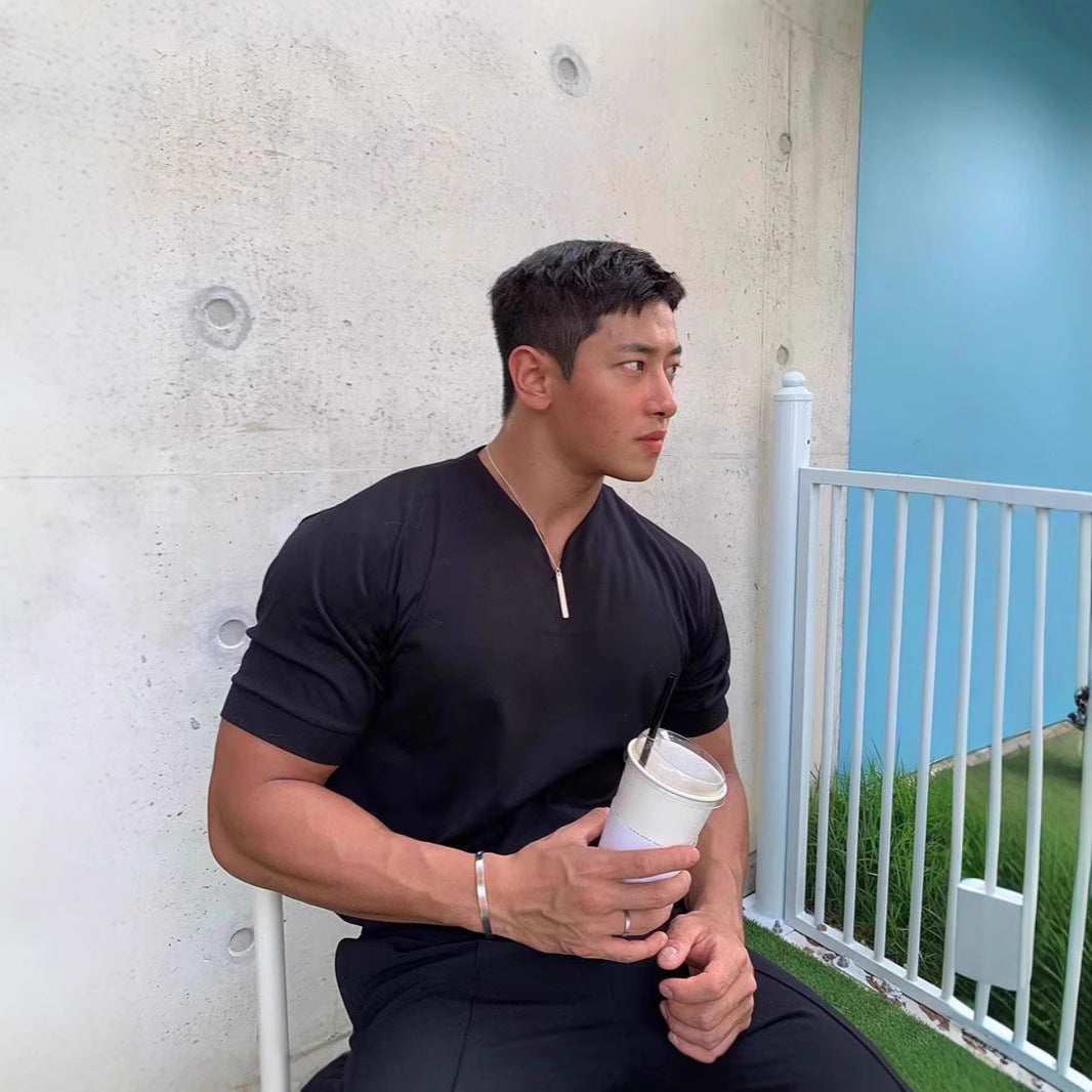 Man in black shirt holding a cup against a concrete wall with a white railing and blue sky.