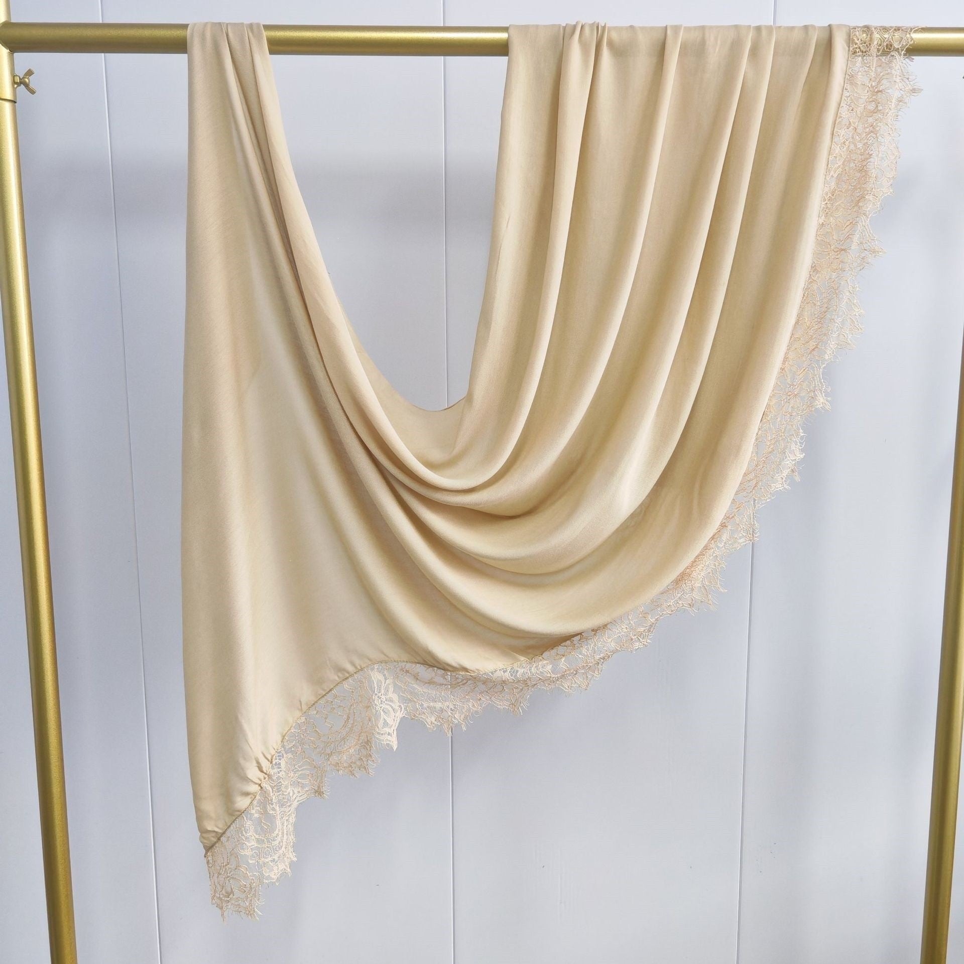 Beige scarf with lace trim draped over a gold rod against a white background