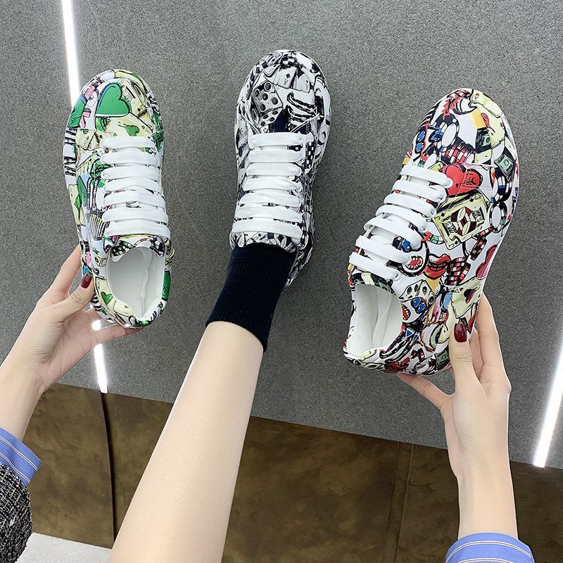 Colorful sneakers with cartoon designs held by a person against a gray background