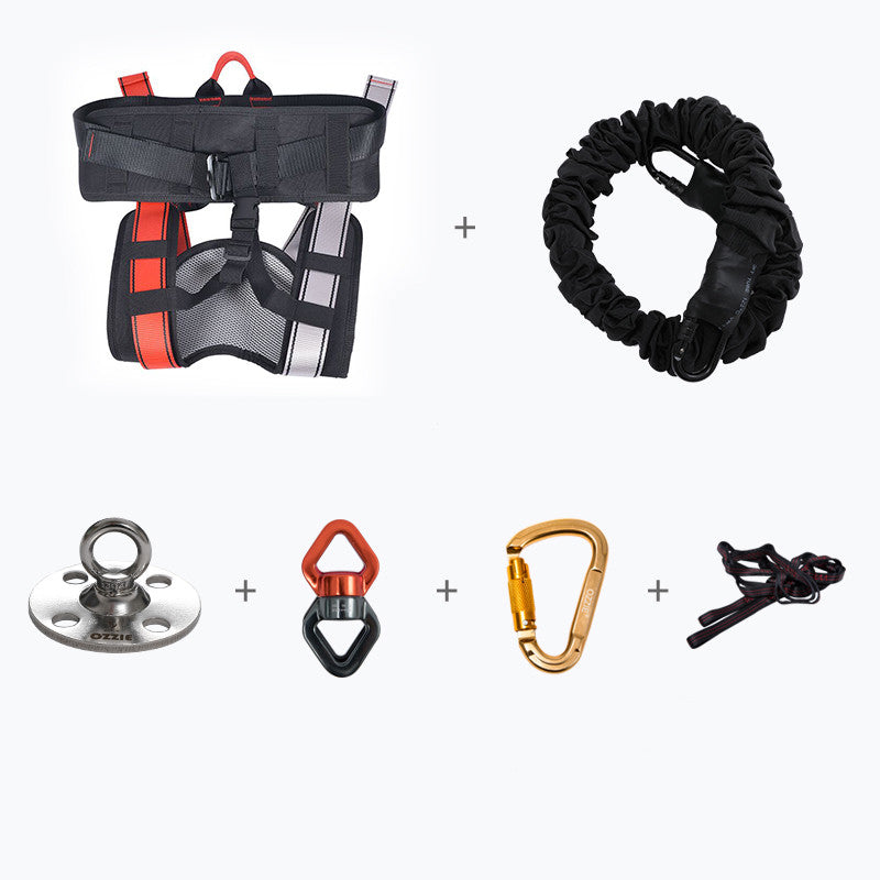 A multi-piece climbing or rescue harness kit on a white background, featuring a black harness with red and gray accents, a black elastic rope, a silver metal anchor plate, a red and black quick-release belting clip, a gold carabiner, and a black rope tool.