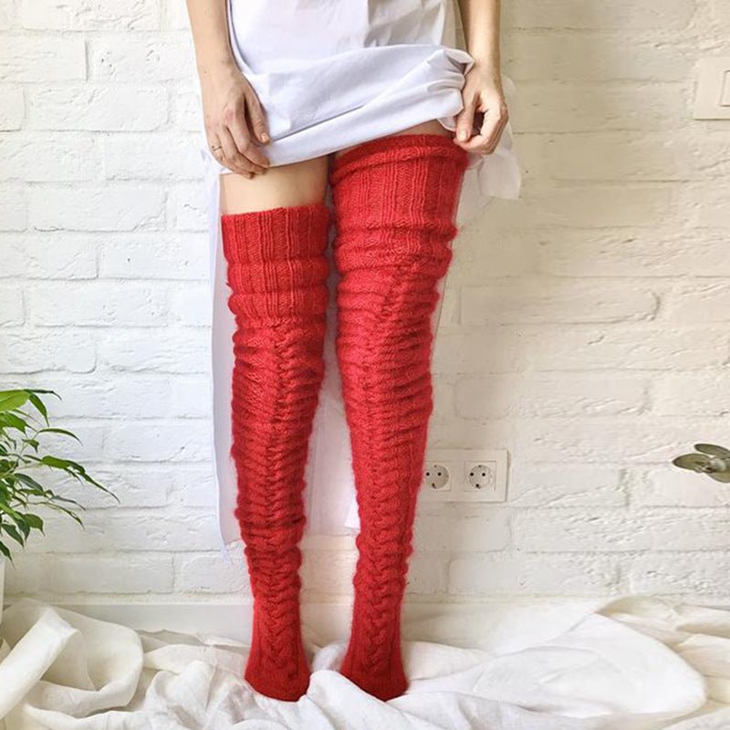 Person wearing red knitted thigh-high socks against a white brick wall.