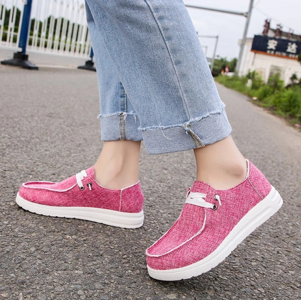 Pink sneakers worn with light blue jeans on a road.