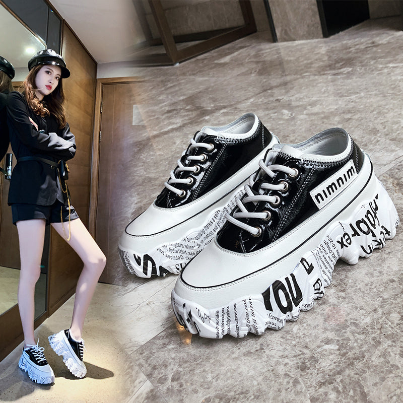 Black and white platform sneakers with text design on a gray floor.