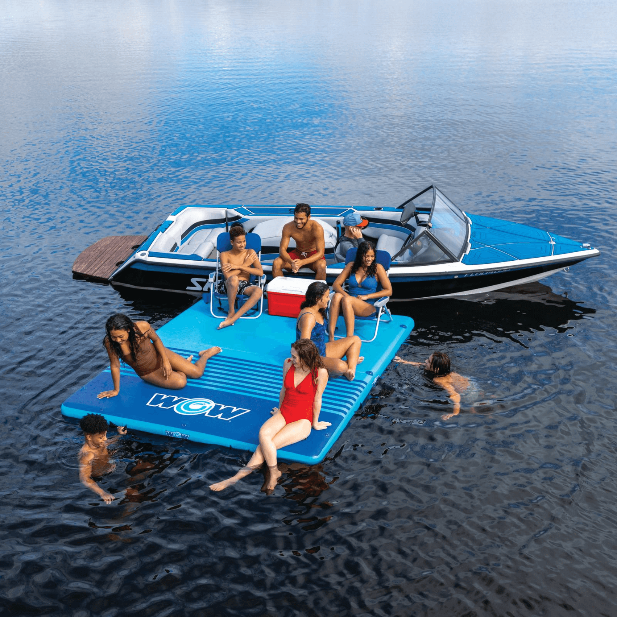 People enjoying a day on a blue inflatable platform with a boat in the background on calm water.