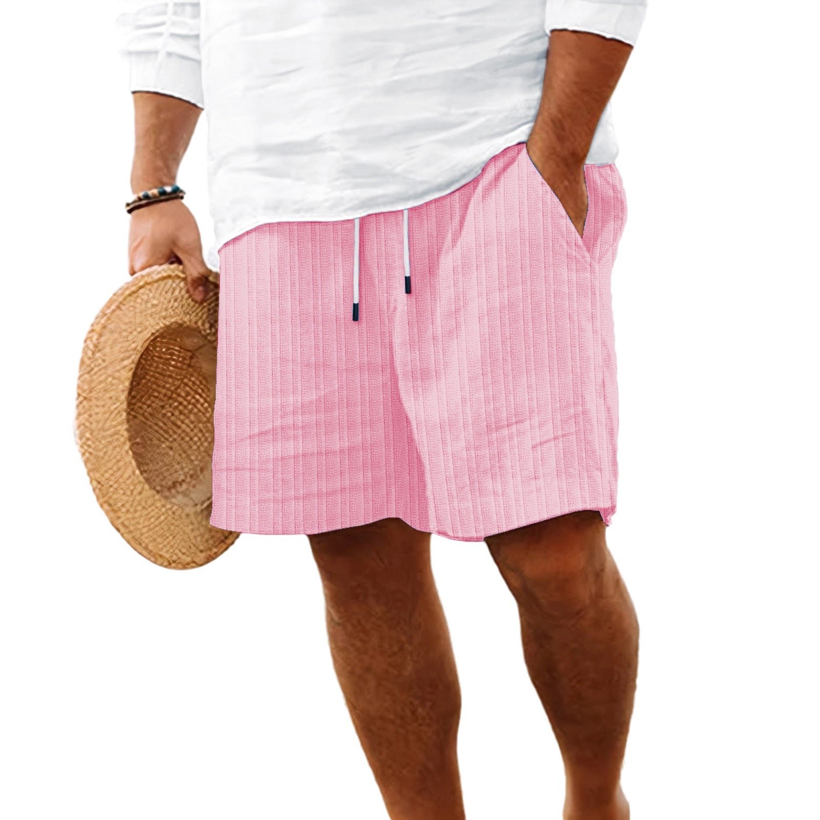 A person wearing pink vertically striped drawstring shorts, a white long-sleeve top, and holding a straw hat against a plain white background.