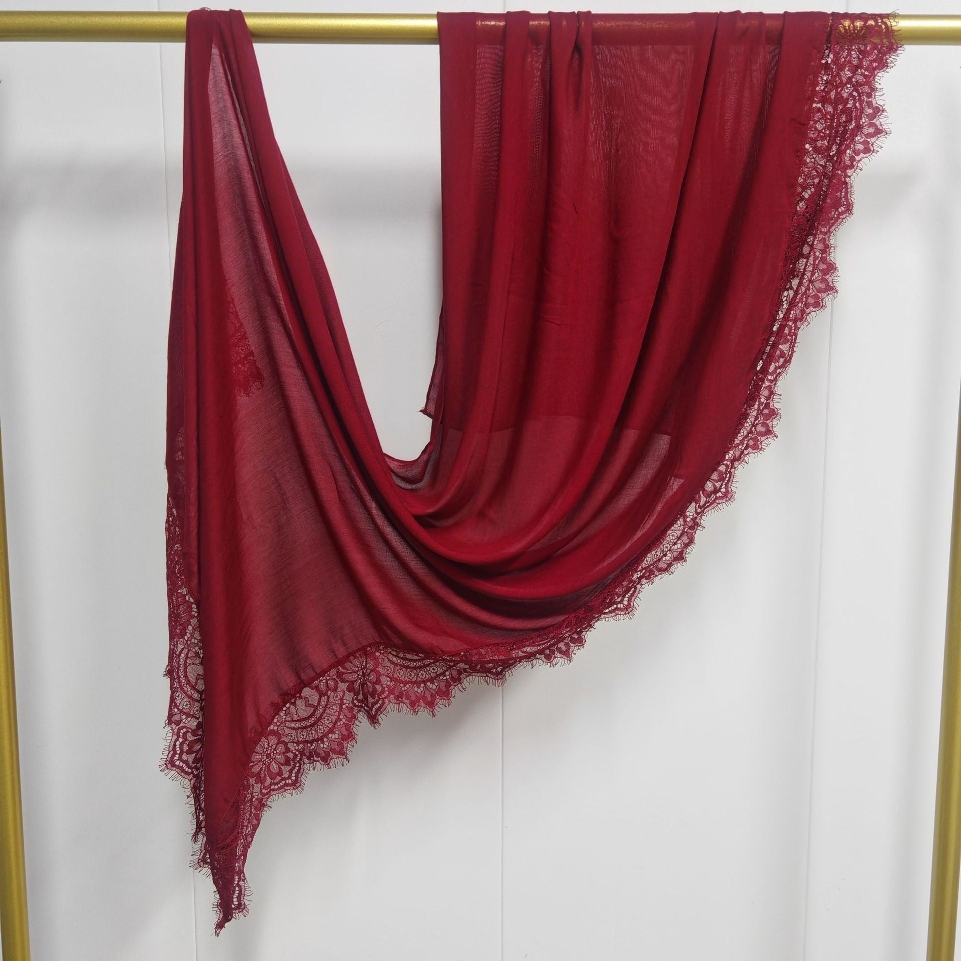 Red scarf with lace trim draped over a gold rod on a white background
