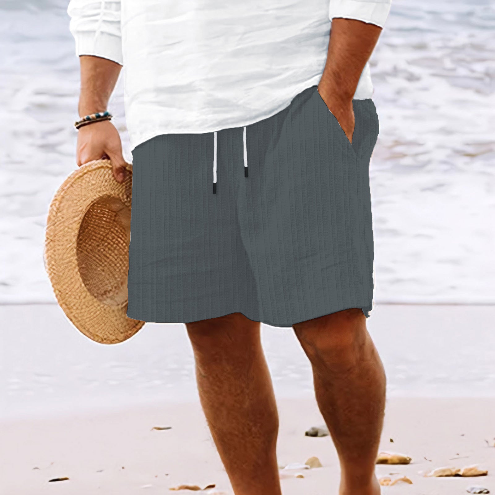 Person wearing gray shorts and holding a straw hat on a beach.