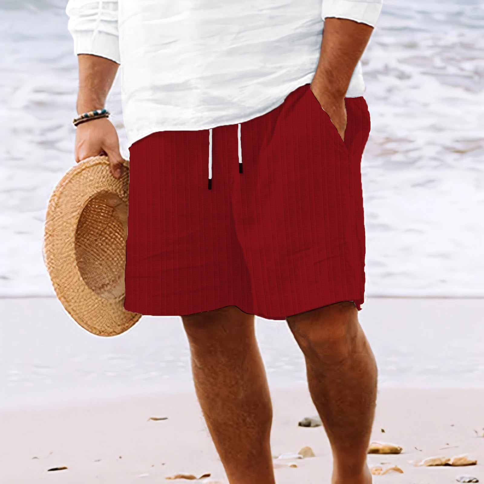 Person wearing red shorts and a white shirt on a beach, holding a straw hat.