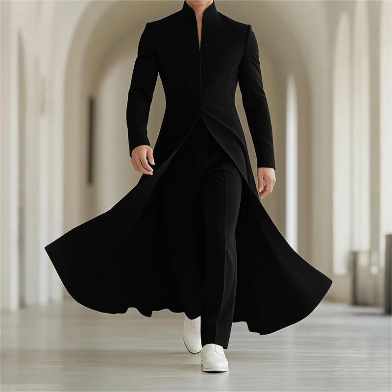A person wearing a long black formal coat with a high collar, black trousers, and white sneakers walking through a bright, softly blurred arched hallway.