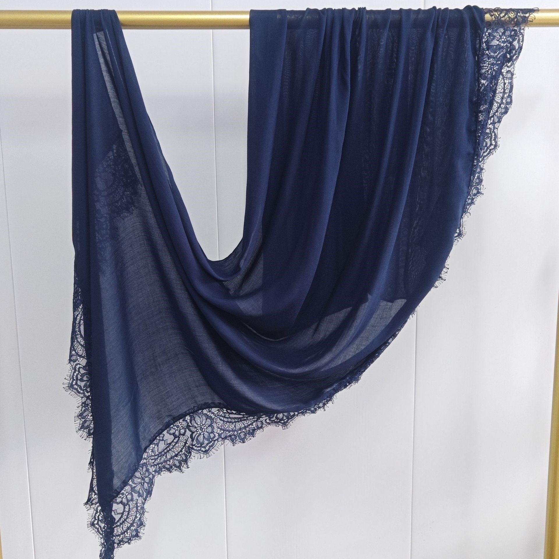 Navy blue scarf with lace edges draped over a gold rod on a white background