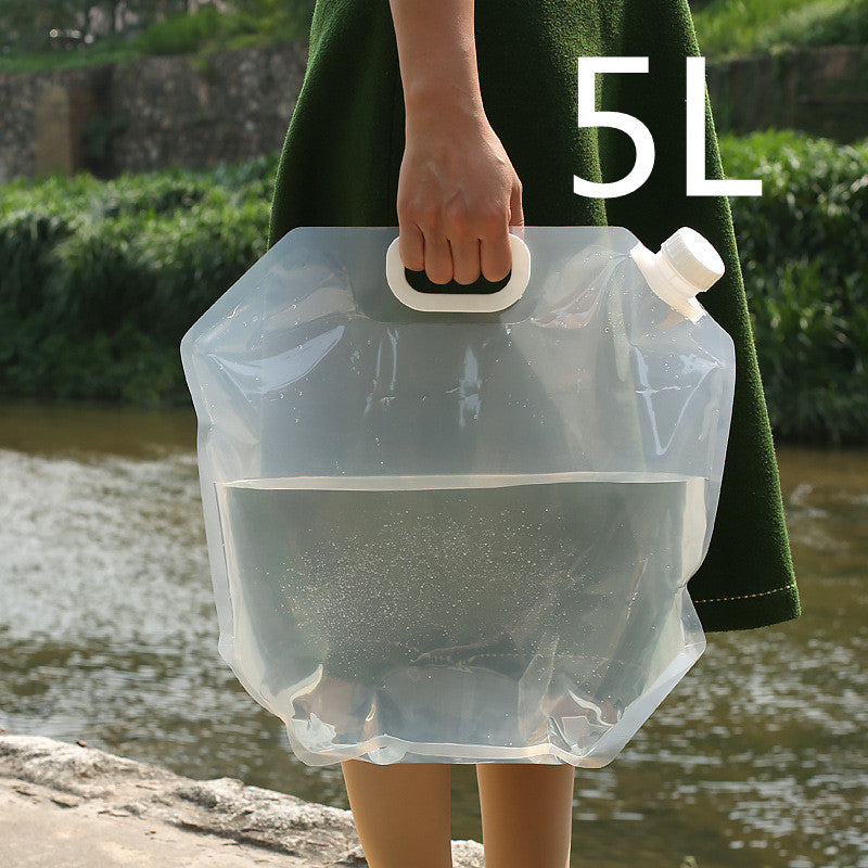 Person holding a transparent 5L water bag outdoors by a body of water.