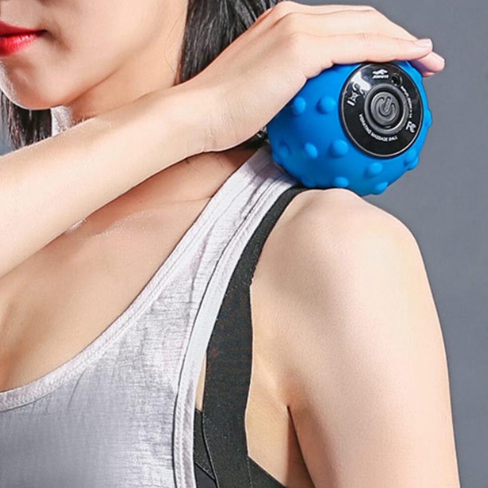 Person using a blue massage ball on their shoulder against a gray background