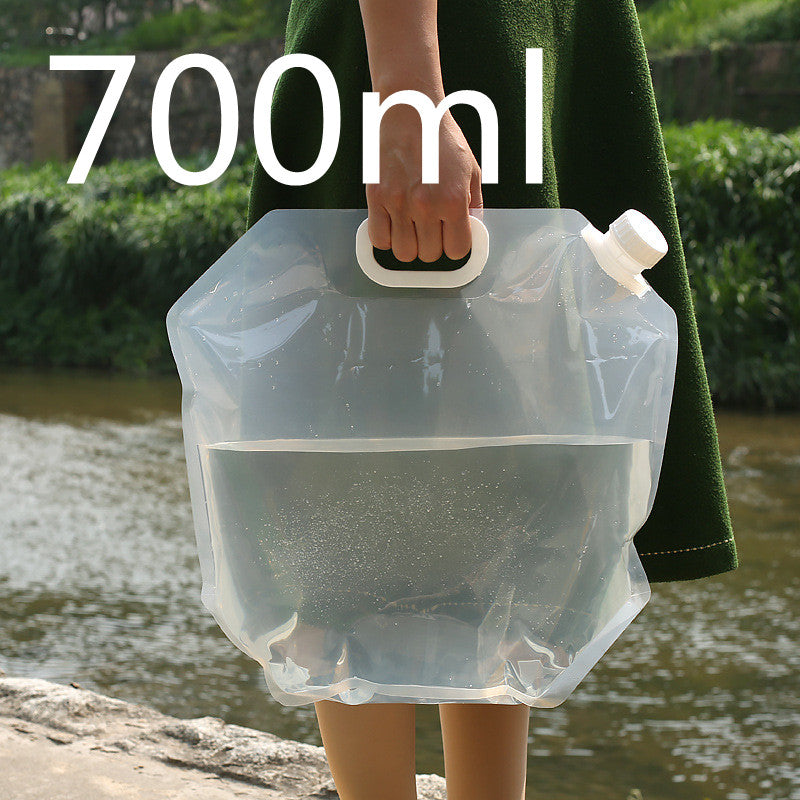 Person holding a transparent water container with a handle, outdoors near a body of water.