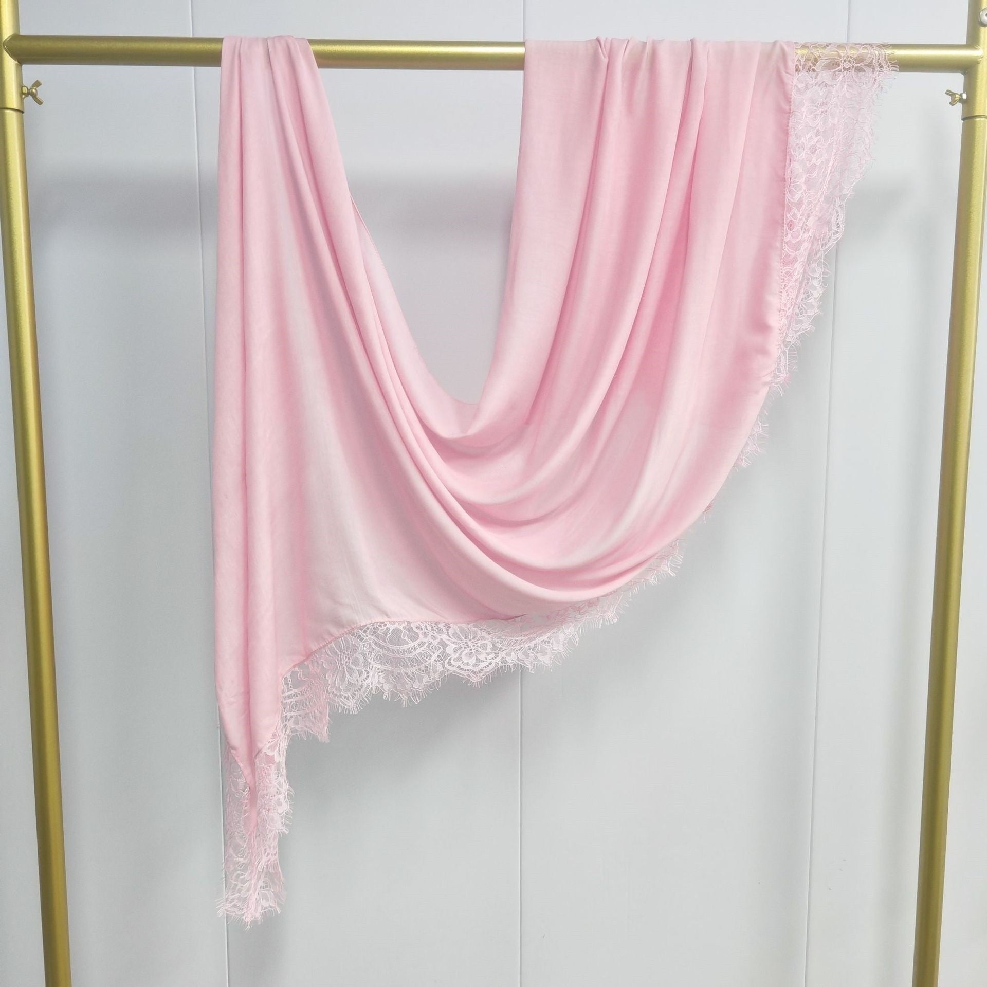 Pink scarf with lace trim draped over a gold frame against a white background