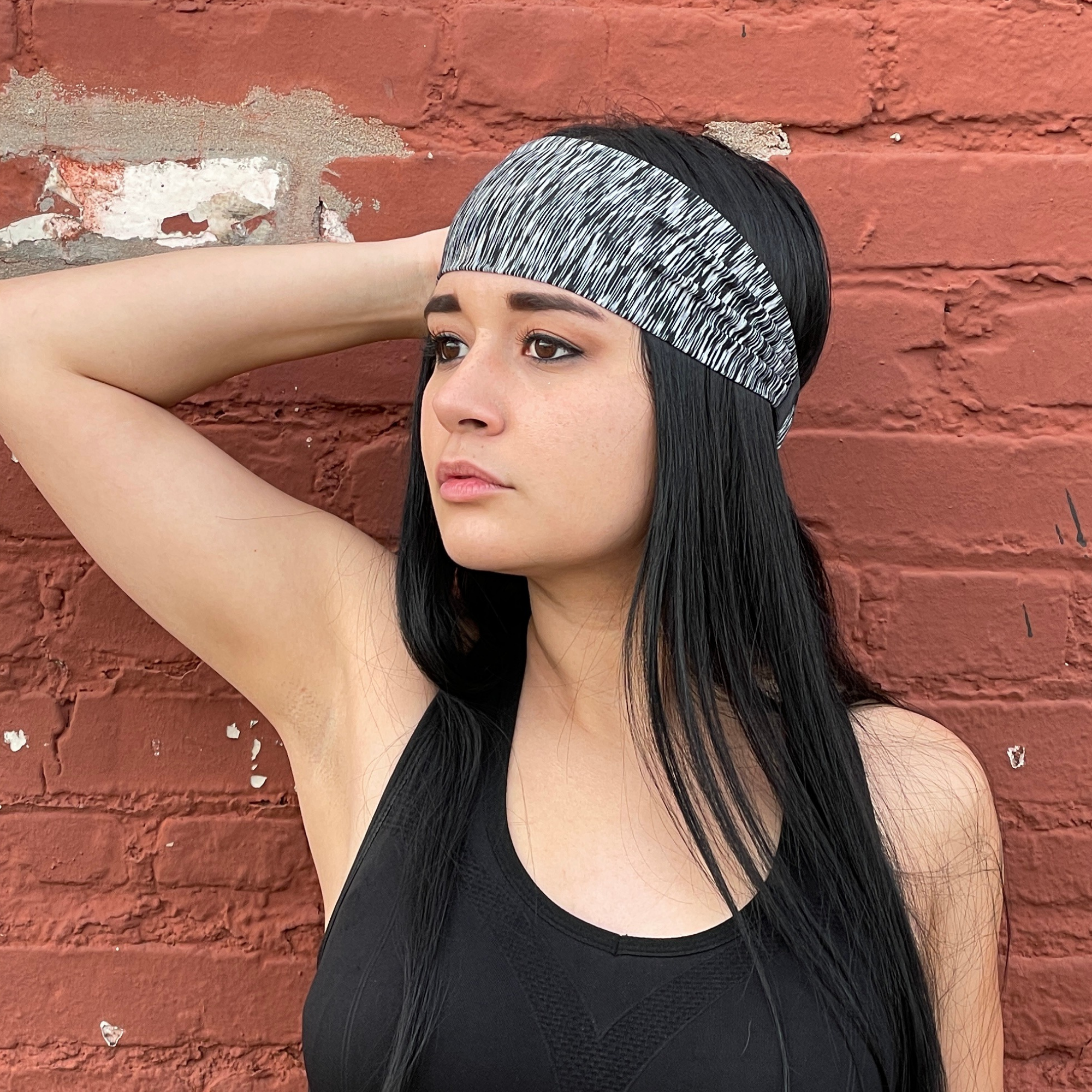 Woman wearing a black tank top and gray headband against a red brick wall.
