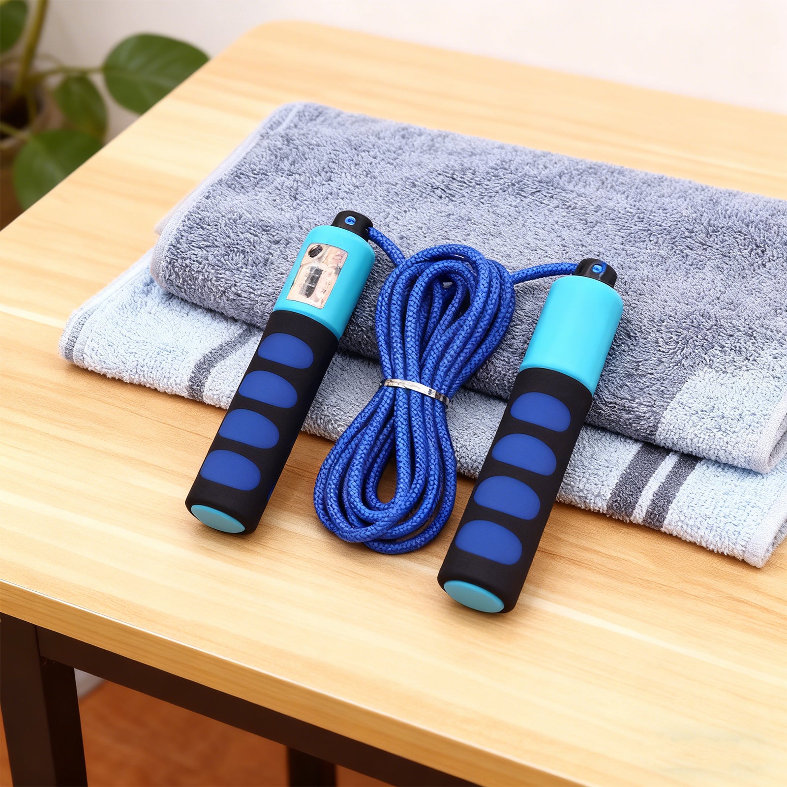 Blue jump rope with black handles on a wooden table with gray towels.