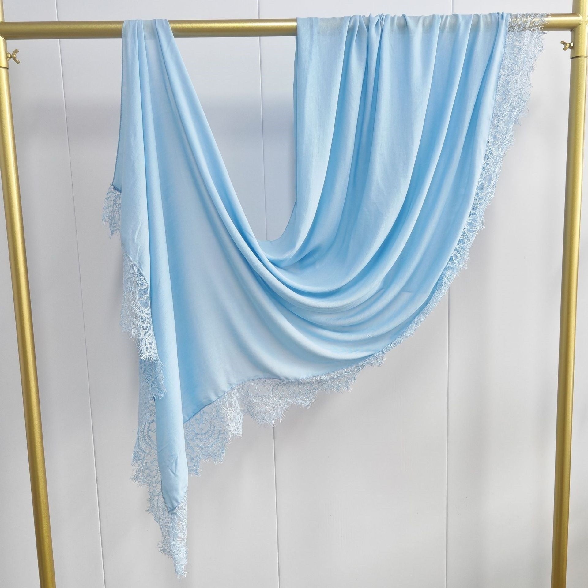 Light blue scarf with lace trim draped over a gold rack on a white background