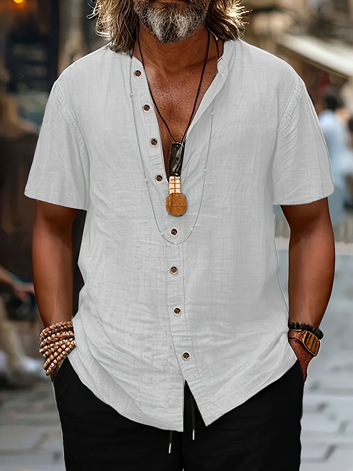 Man wearing a white short-sleeve shirt with buttons, black pants, and multiple necklaces and bracelets.