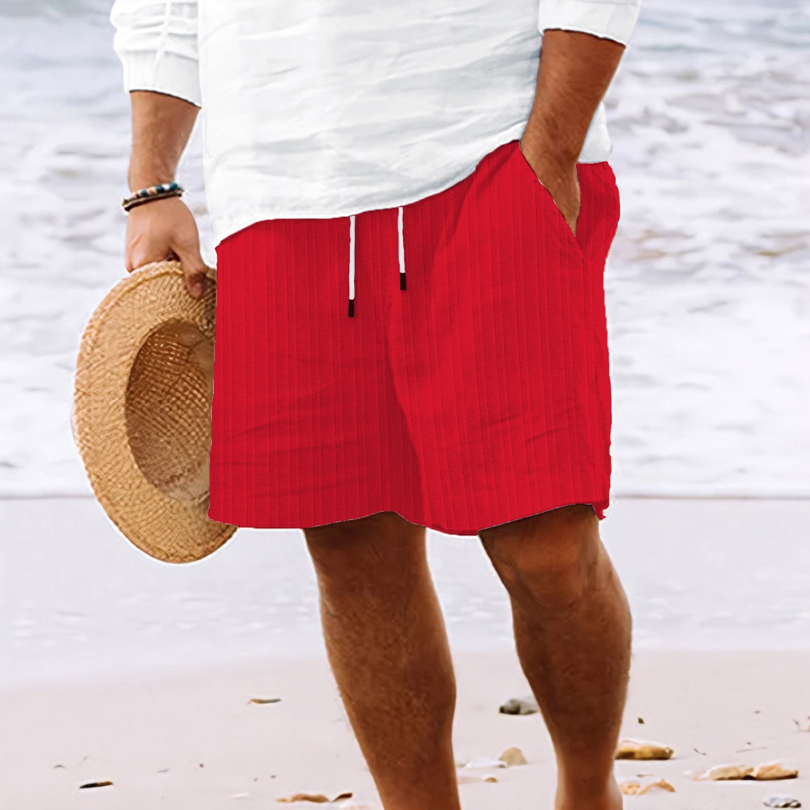 Person wearing red shorts and a white shirt on a beach, holding a straw hat.