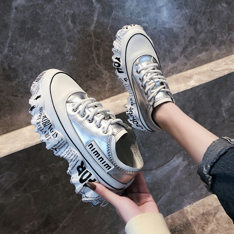Silver sneakers with ruffled details held by a person on a stone floor.