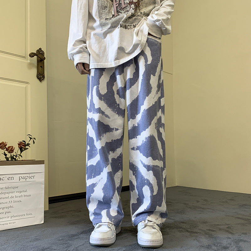 Person wearing a white sweatshirt and blue camouflage pants in a room with a door and plant.