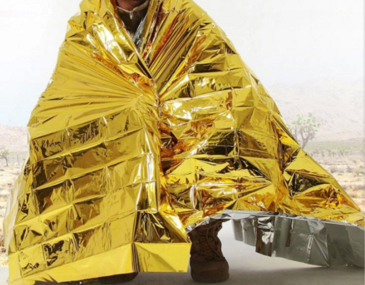Person wrapped in a gold reflective emergency blanket with a blurred outdoor background