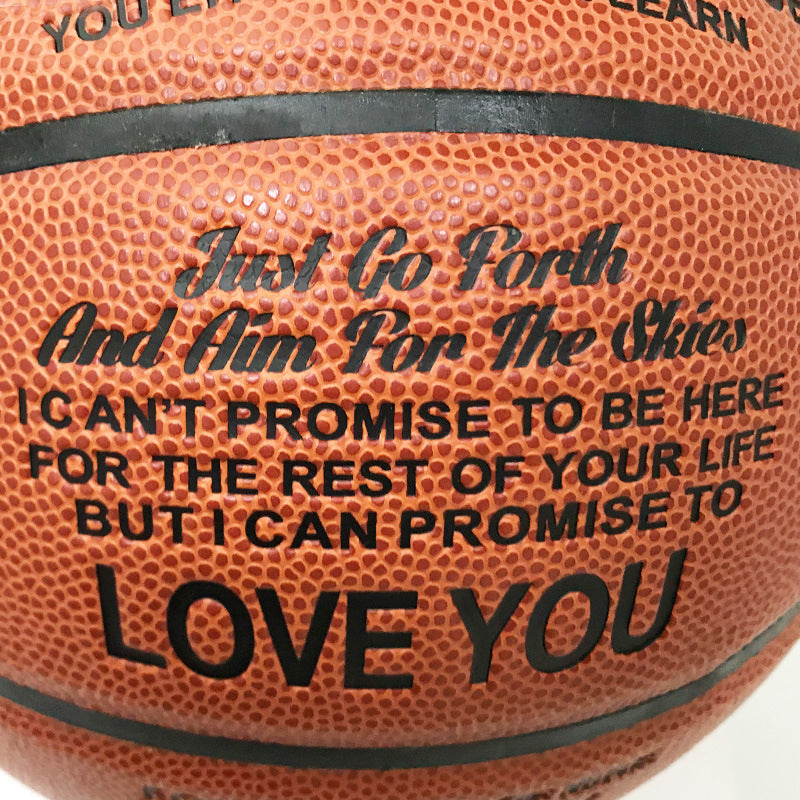 Close-up of a basketball with printed black text reading 'Just Go Forth And Aim For The Stars' and 'I CAN'T PROMISE TO BE HERE FOR THE REST OF YOUR LIFE BUT I CAN PROMISE TO LOVE YOU'.