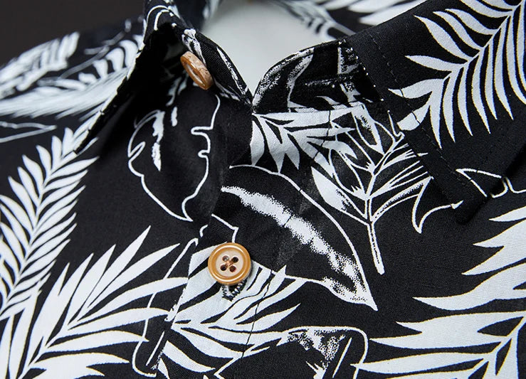 Close-up of a black shirt with white leaf pattern and a button, featuring a tropical design.