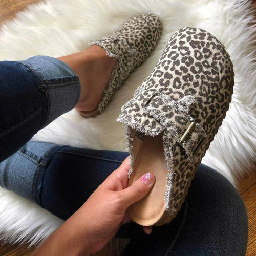 Leopard print loafers with embellishments on a fluffy white surface.