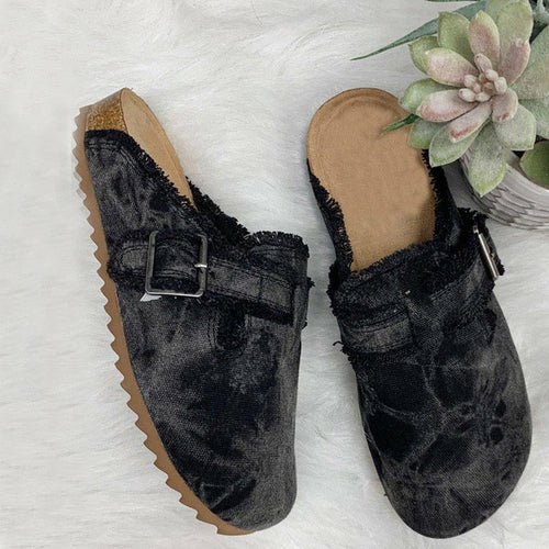 Pair of black velvet mules with buckles on a textured white surface.