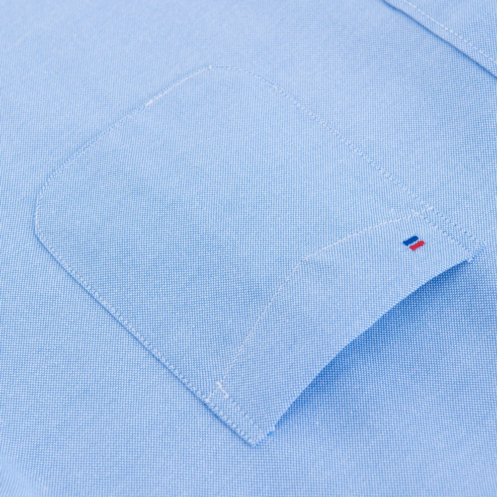 Close-up of a light blue shirt with a small logo on the chest pocket.