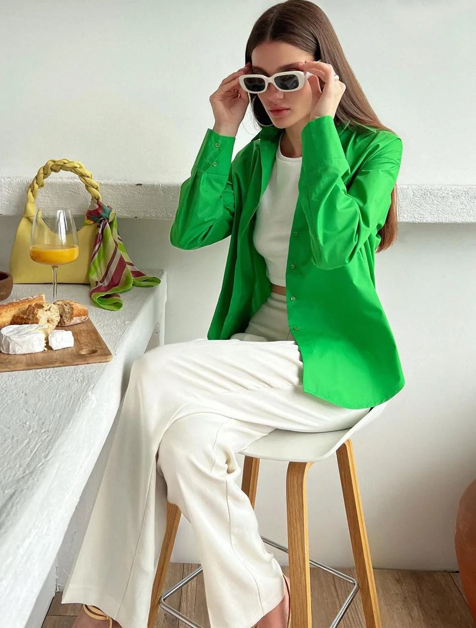 Woman in a green blazer and white pants sitting on a stool in a kitchen.