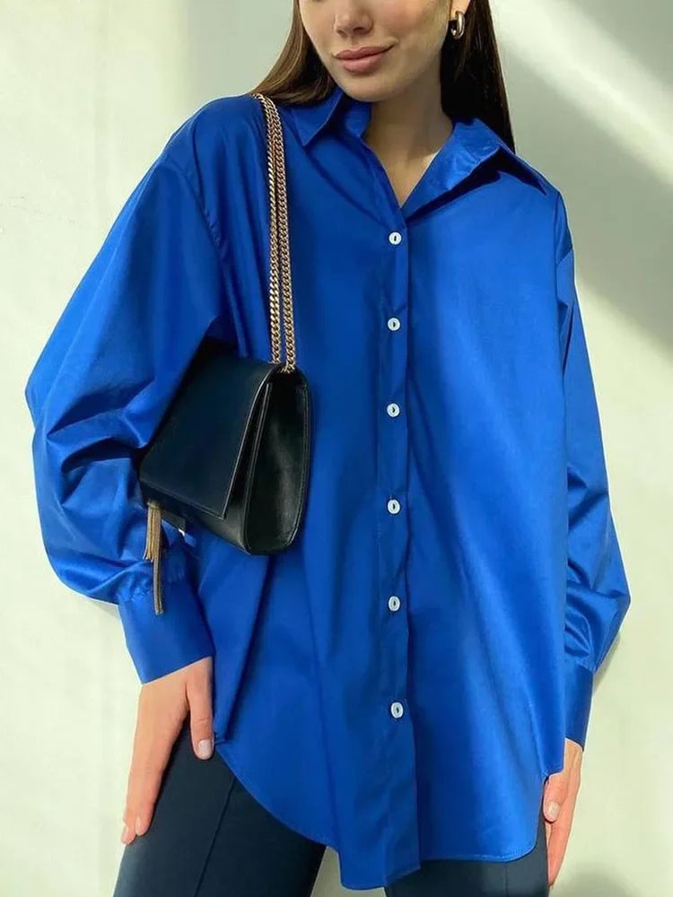 Person wearing a blue shirt holding a black handbag against a neutral background