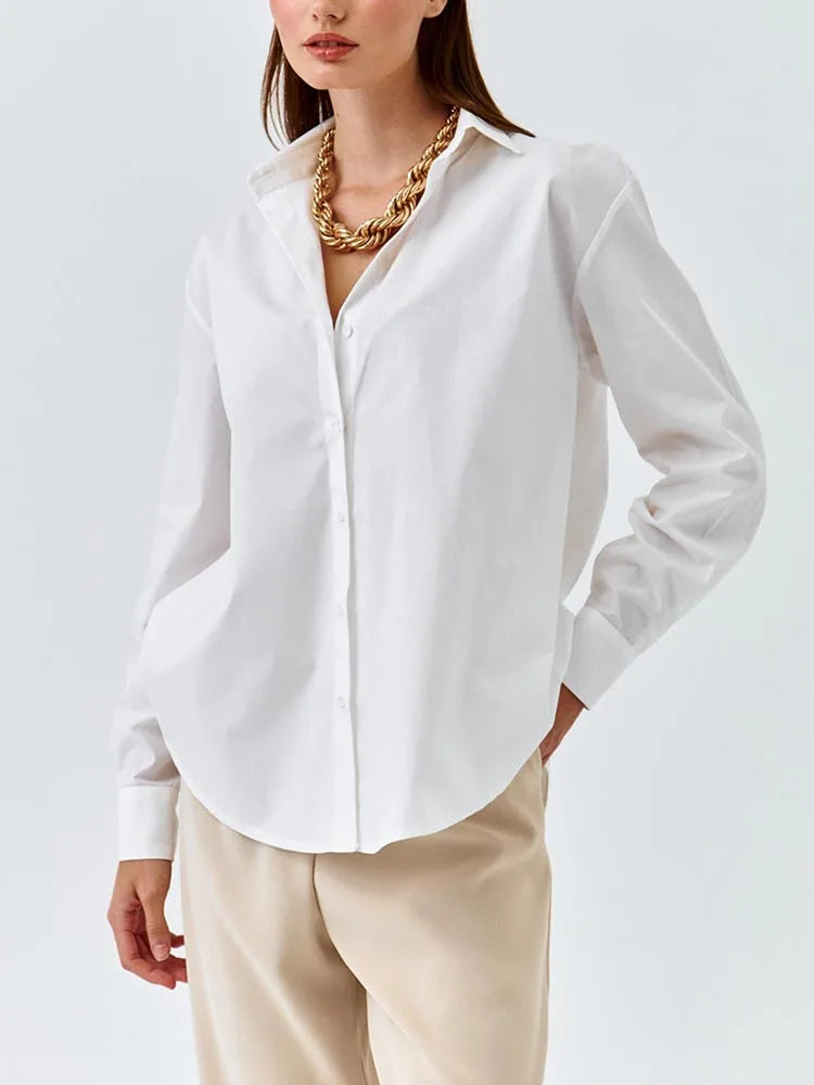 Person wearing a white shirt and beige pants with a gold necklace on a light gray background
