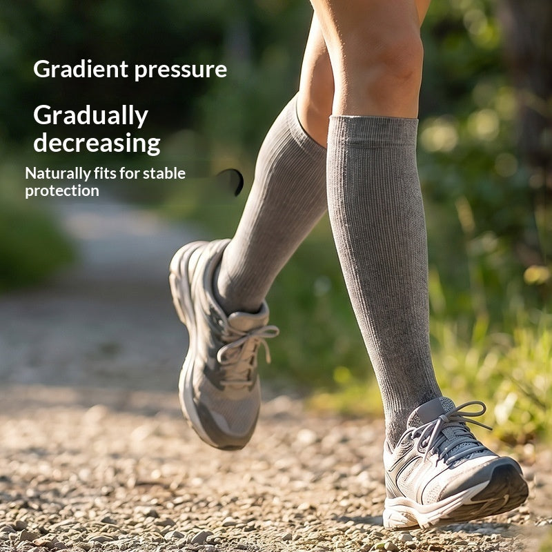 A person outdoors wearing gray knee-high compression socks and hiking shoes on a gravel path, with text on the left reading 'Gradient pressure', 'Gradually decreasing', and 'Naturally fits for stable protection'.