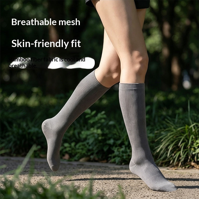 A person outdoors wearing a pair of knee-high gray socks on a path with green foliage in the background. White text on the left reads 'Breathable mesh' and 'Skin-friendly fit'.