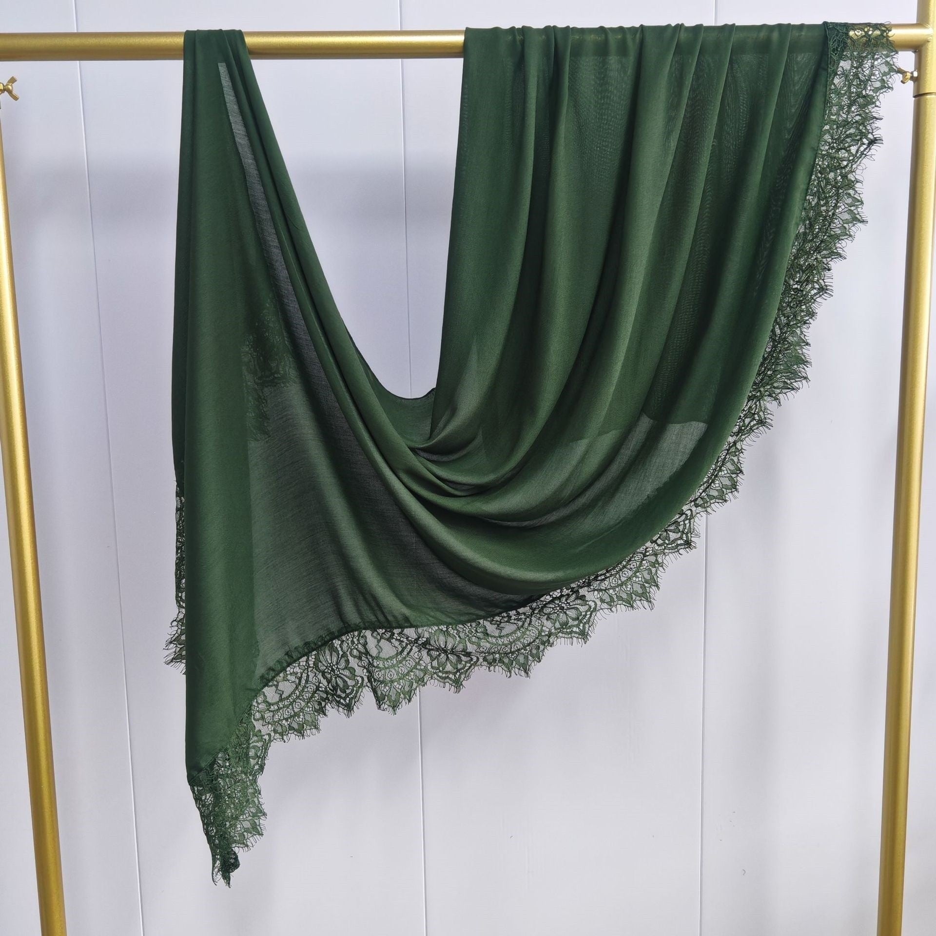 Green scarf with lace trim draped over a gold rod against a white background