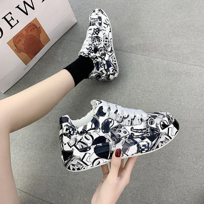White sneakers with black abstract pattern worn by a person on a gray floor.
