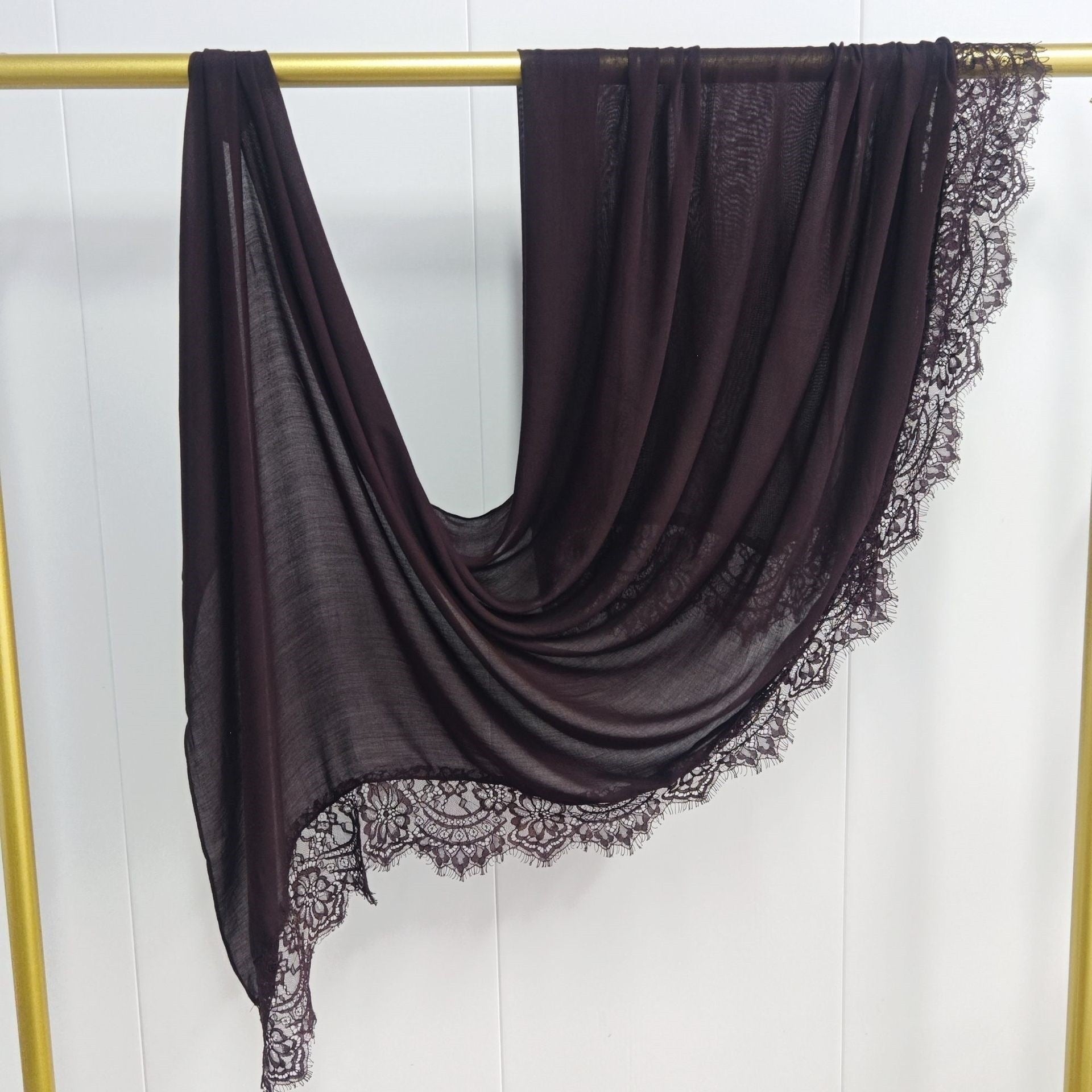 Dark brown scarf with lace trim draped over a gold rod on a white background